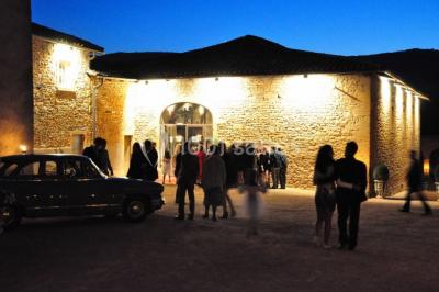 Cour éclairée au crépuscule avec des bâtiments en pierre, des torches allumées et des personnes en arrière-plan.