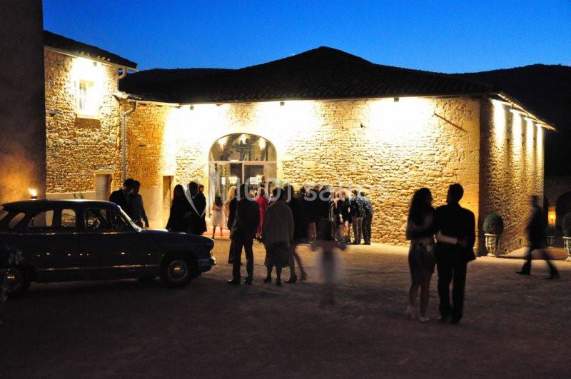 Groupe de personnes rassemblées devant un bâtiment en pierre éclairé, à la tombée de la nuit.
