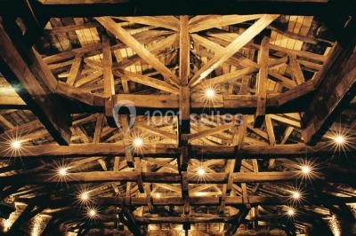 Cour éclairée au crépuscule avec des bâtiments en pierre, des torches allumées et des personnes en arrière-plan.