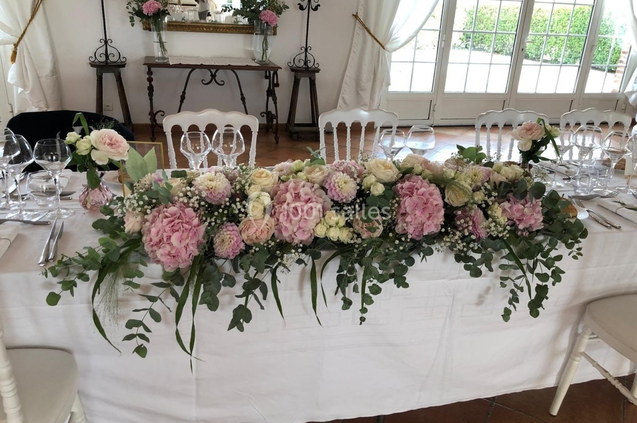 Décoration florale composée de roses et hortensias roses et blancs, disposée sur une table de réception élégante.