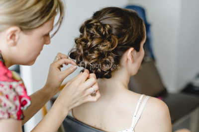 Femme en robe en dentelle blanche, coiffée d'une tresse et d'une fleur, dans un intérieur lumineux.