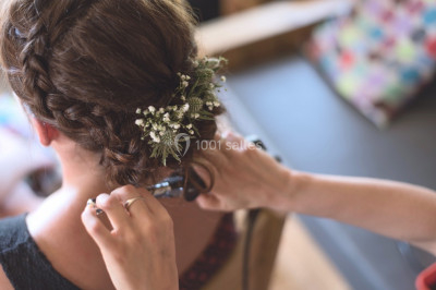 Femme en robe en dentelle blanche, coiffée d'une tresse et d'une fleur, dans un intérieur lumineux.