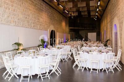 Façade vitrée d'un bâtiment moderne avec éclairages rouges, intégrée à des murs en pierre ancienne.