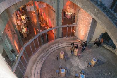 Façade vitrée d'un bâtiment moderne avec éclairages rouges, intégrée à des murs en pierre ancienne.