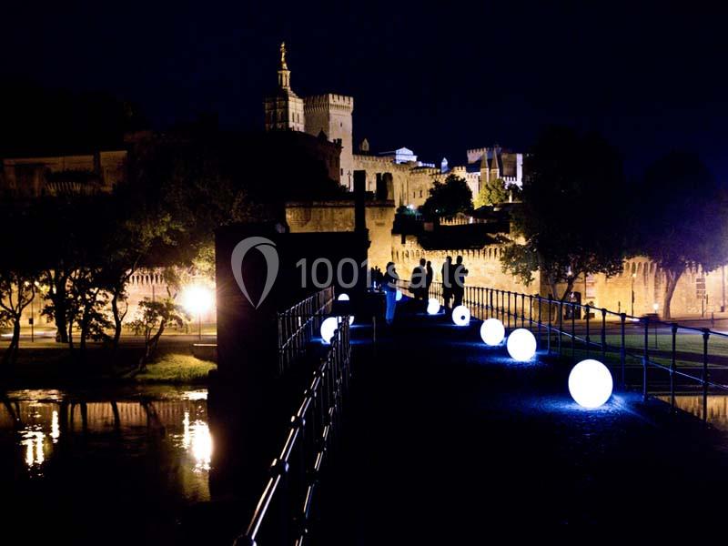 Pont illuminé la nuit avec des sphères lumineuses, vue sur des bâtiments historiques en arrière-plan.
