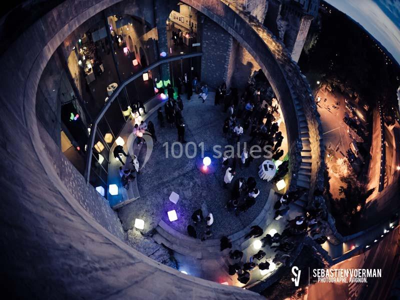 Vue plongeante d'une cour circulaire illuminée par des lampes colorées, avec des invités rassemblés en soirée.