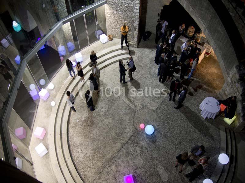 Vue plongeante sur un espace circulaire avec des marches, des personnes discutant et des lumières colorées dispersées.