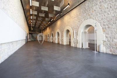 Façade vitrée d'un bâtiment moderne avec éclairages rouges, intégrée à des murs en pierre ancienne.