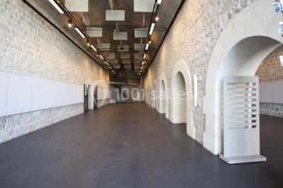 Façade vitrée d'un bâtiment moderne avec éclairages rouges, intégrée à des murs en pierre ancienne.