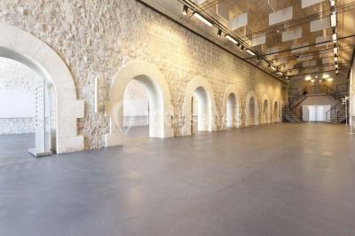 Façade vitrée d'un bâtiment moderne avec éclairages rouges, intégrée à des murs en pierre ancienne.