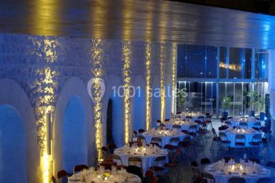 Façade vitrée d'un bâtiment moderne avec éclairages rouges, intégrée à des murs en pierre ancienne.