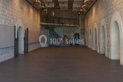 Façade vitrée d'un bâtiment moderne avec éclairages rouges, intégrée à des murs en pierre ancienne.