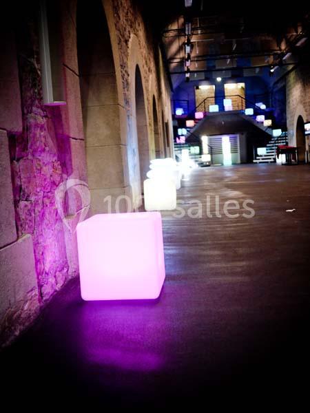 Des cubes lumineux colorés éclairent un couloir voûté en pierre avec un sol sombre.