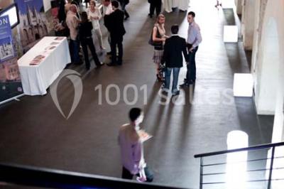 Façade vitrée d'un bâtiment moderne avec éclairages rouges, intégrée à des murs en pierre ancienne.