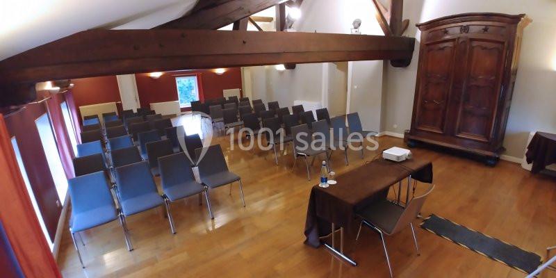 Salle de réunion avec parquet, rangées de chaises, table équipée d’un projecteur et armoire en bois en arrière-plan.