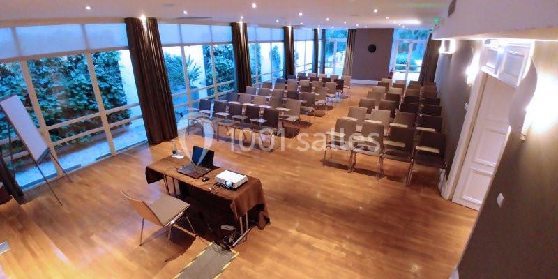Salle de conférence lumineuse avec parquet, chaises alignées, table équipée d'un ordinateur et grandes baies vitrées.