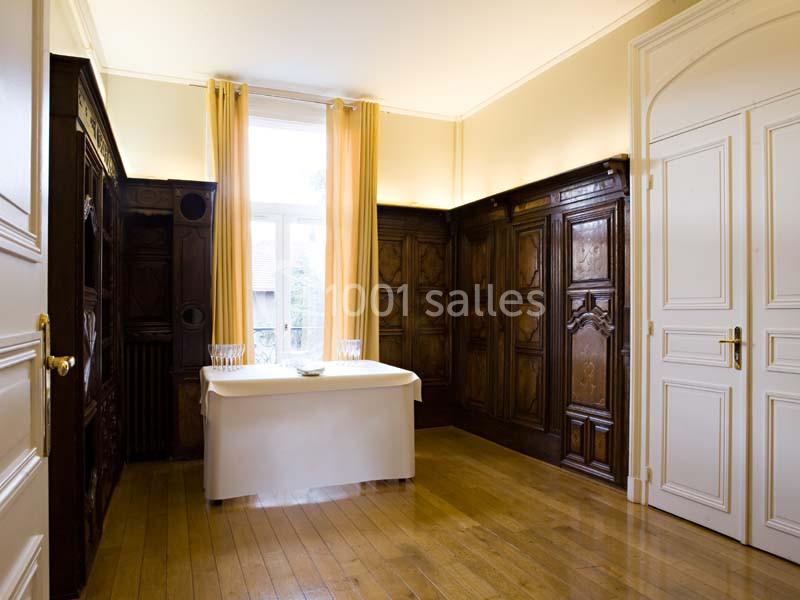Une pièce lumineuse avec parquet, boiseries murales sculptées, rideaux beiges et une table blanche centrale.