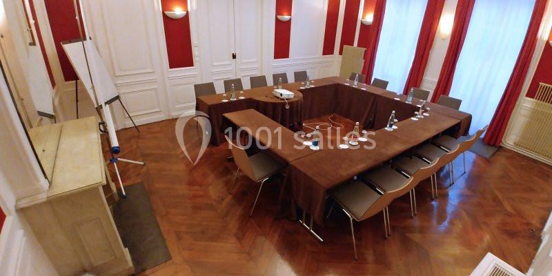 Salle de réunion avec table en U, chaises, vidéoprojecteur, tableau blanc et murs rouges et blancs.