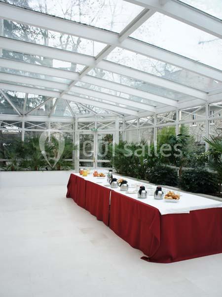 Table dressée avec nappe rouge, contenant des boissons et viennoiseries, dans une salle lumineuse entourée de plantes.