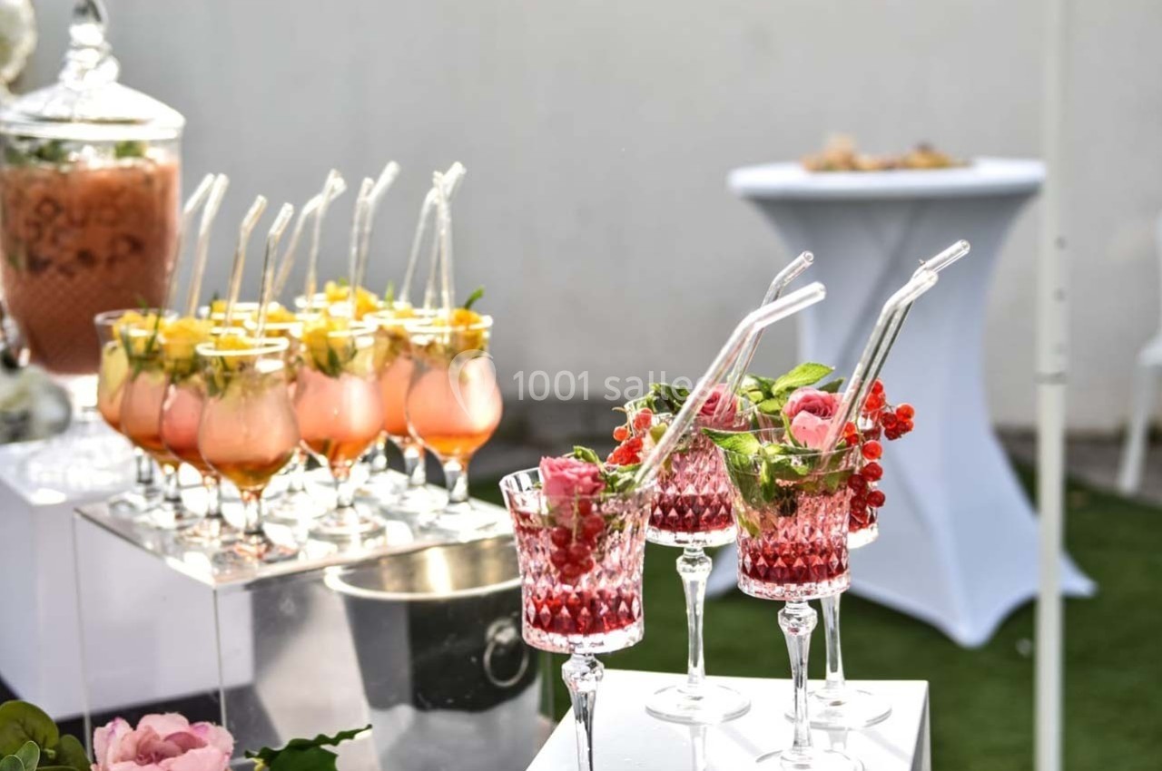 Verres de cocktails colorés garnis de fruits et de feuilles, disposés sur une table lors d'un événement en extérieur.