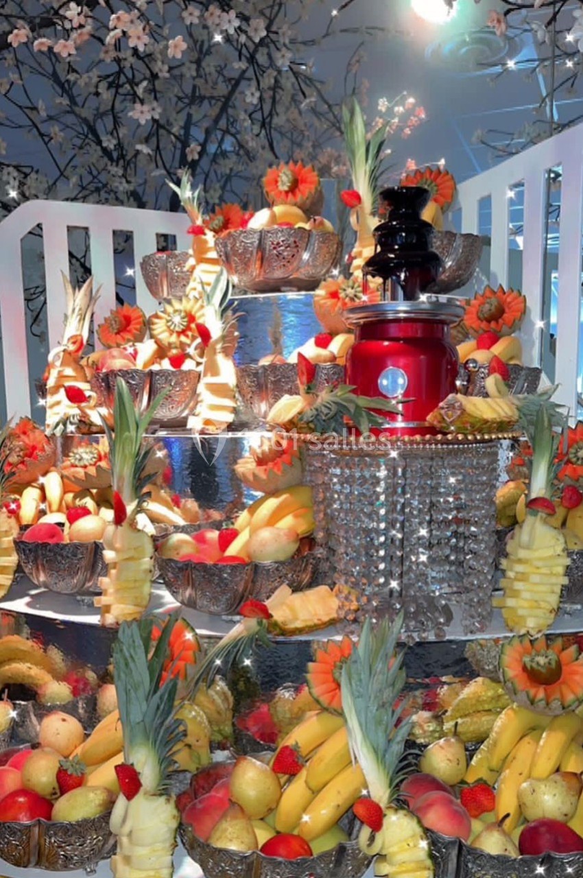 Plateau décoratif avec un assortiment de fruits frais sculptés et disposés autour d'une fontaine rouge.