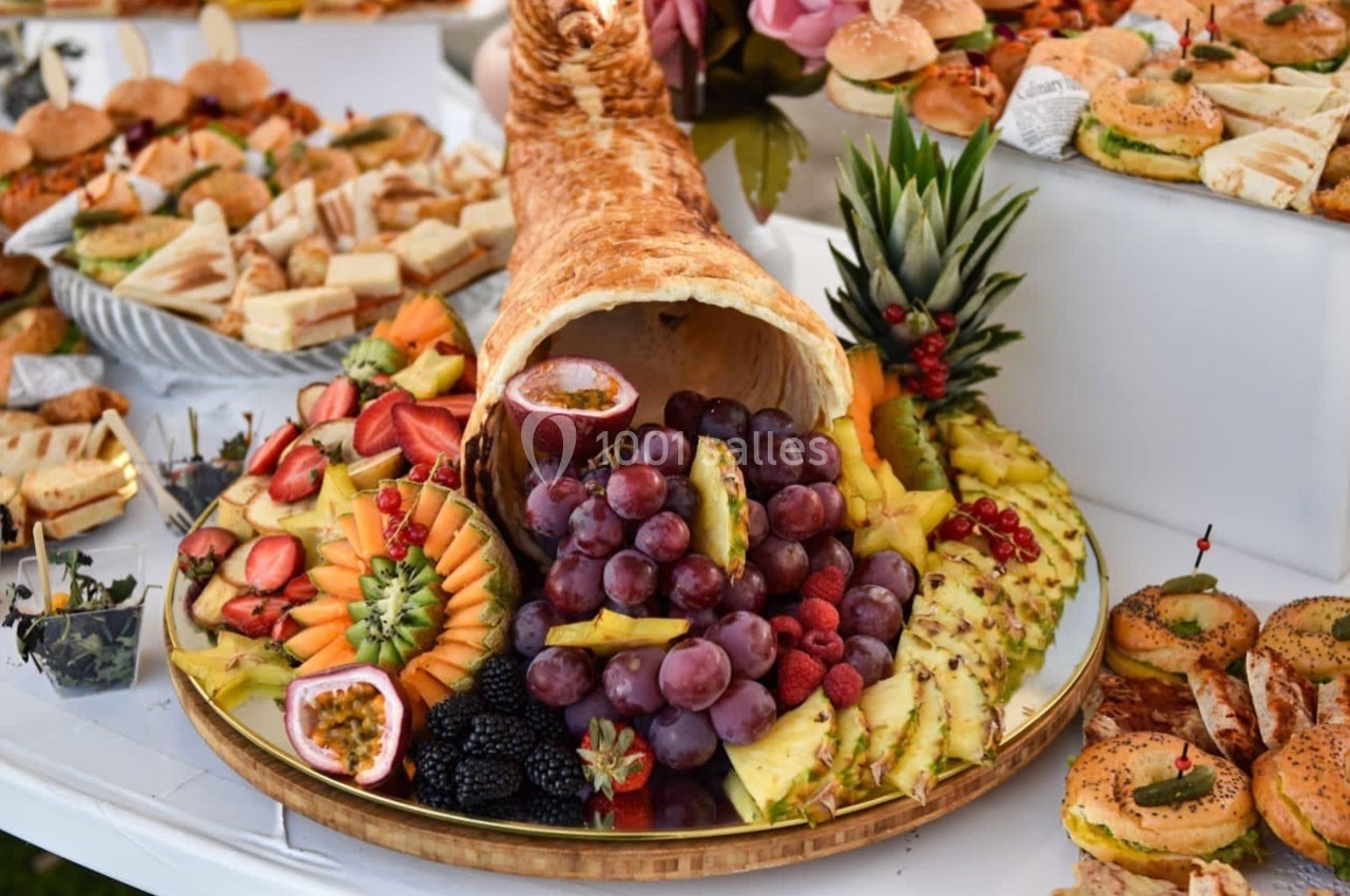 Plateau de fruits variés avec raisins, ananas, fraises et autres, disposés autour d'une corne d'abondance en pain.