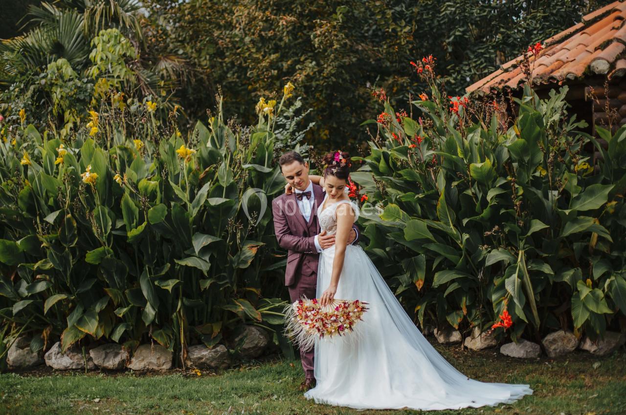 Un couple en tenue de mariage pose devant un jardin luxuriant avec des fleurs colorées.