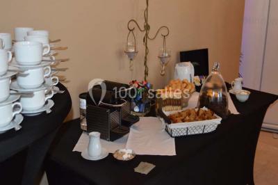 Salle de réception avec tables rondes dressées, nappes blanches, assiettes dorées et décoration florale centrale.