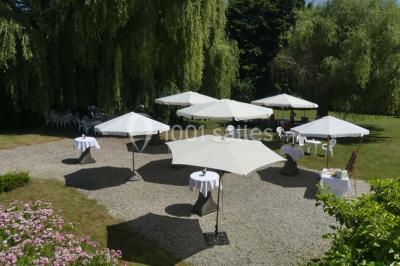 Salle de réception avec tables rondes dressées, nappes blanches, assiettes dorées et décoration florale centrale.
