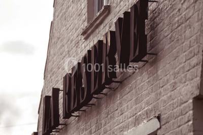 Salle de réception avec tables rondes dressées, nappes blanches, assiettes dorées et décoration florale centrale.