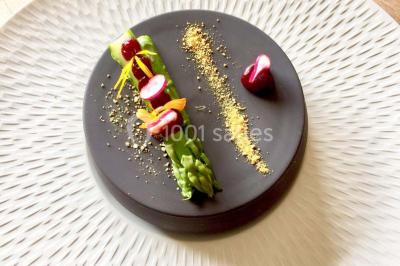 Salle de réception avec tables rondes dressées, nappes blanches, assiettes dorées et décoration florale centrale.