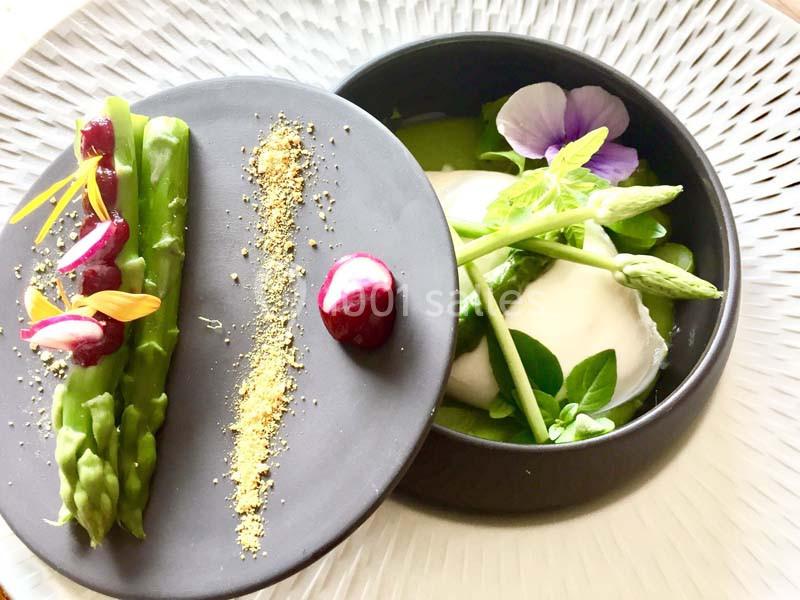 Assiette gastronomique avec asperges, crème, fleurs comestibles et présentation soignée sur une assiette noire.