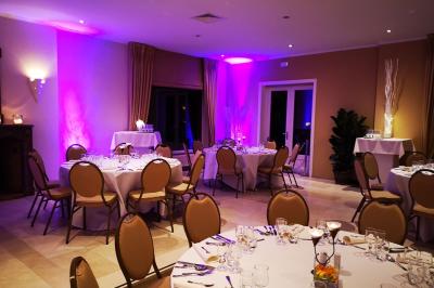 Salle de réception avec tables rondes dressées, nappes blanches, assiettes dorées et décoration florale centrale.