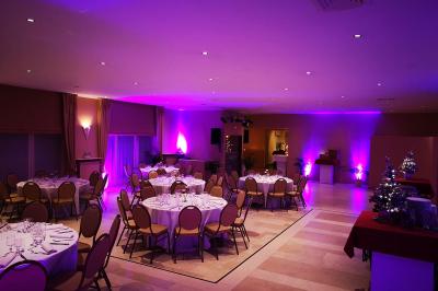 Salle de réception avec tables rondes dressées, nappes blanches, assiettes dorées et décoration florale centrale.