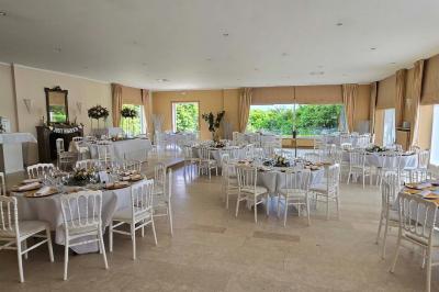 Salle de réception avec tables rondes dressées, nappes blanches, assiettes dorées et décoration florale centrale.