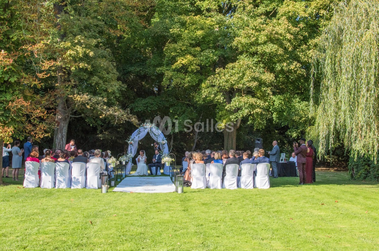 Cérémonie de mariage en plein air avec des invités assis devant une arche décorée, entourée d'arbres verdoyants.
