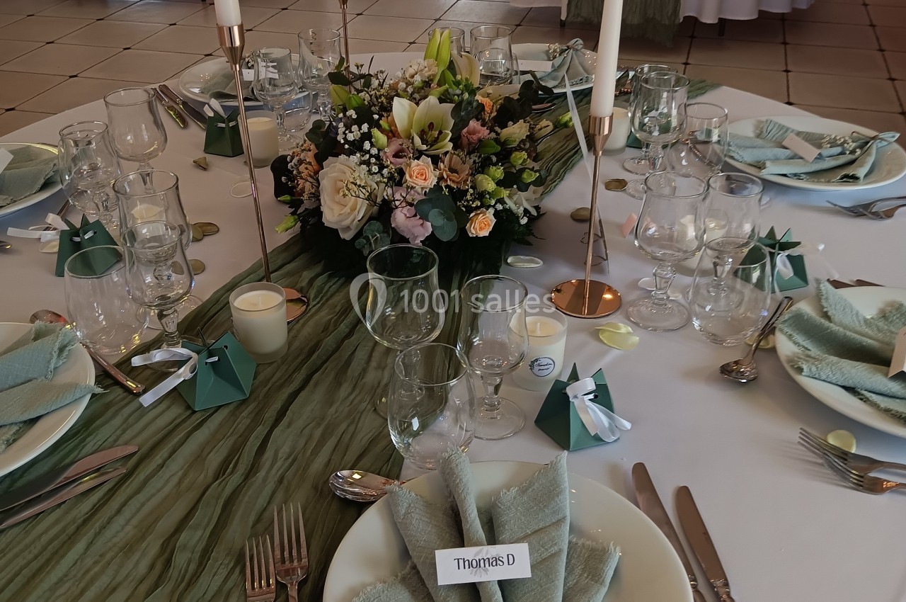 Table élégamment dressée avec nappes vertes, centre de table floral, bougies et pliages de serviettes.