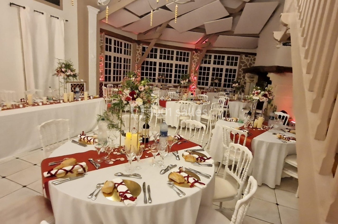 Salle de réception décorée avec des tables rondes, nappes rouges et blanches, et arrangements floraux élégants.