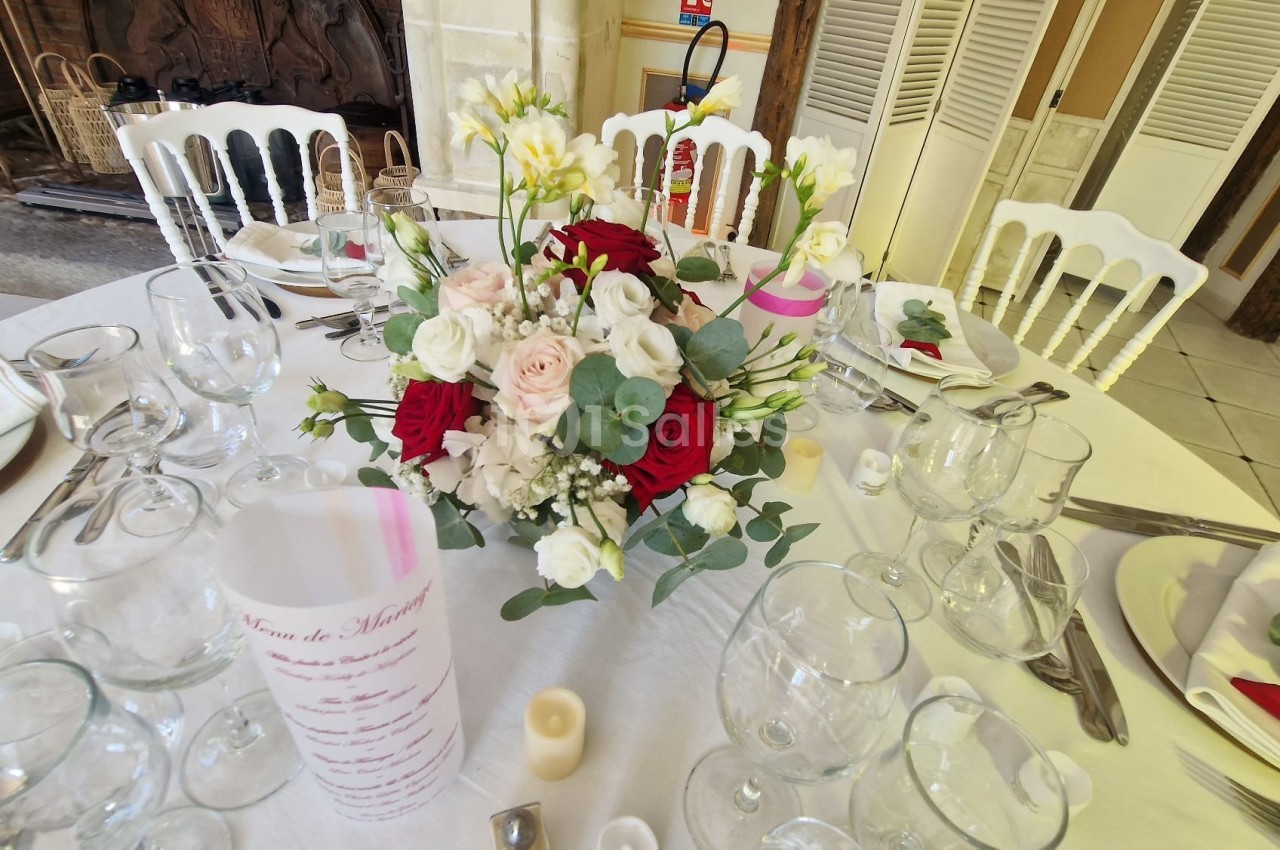 Table dressée pour un événement avec un centre de table floral composé de roses rouges, blanches et feuillage.