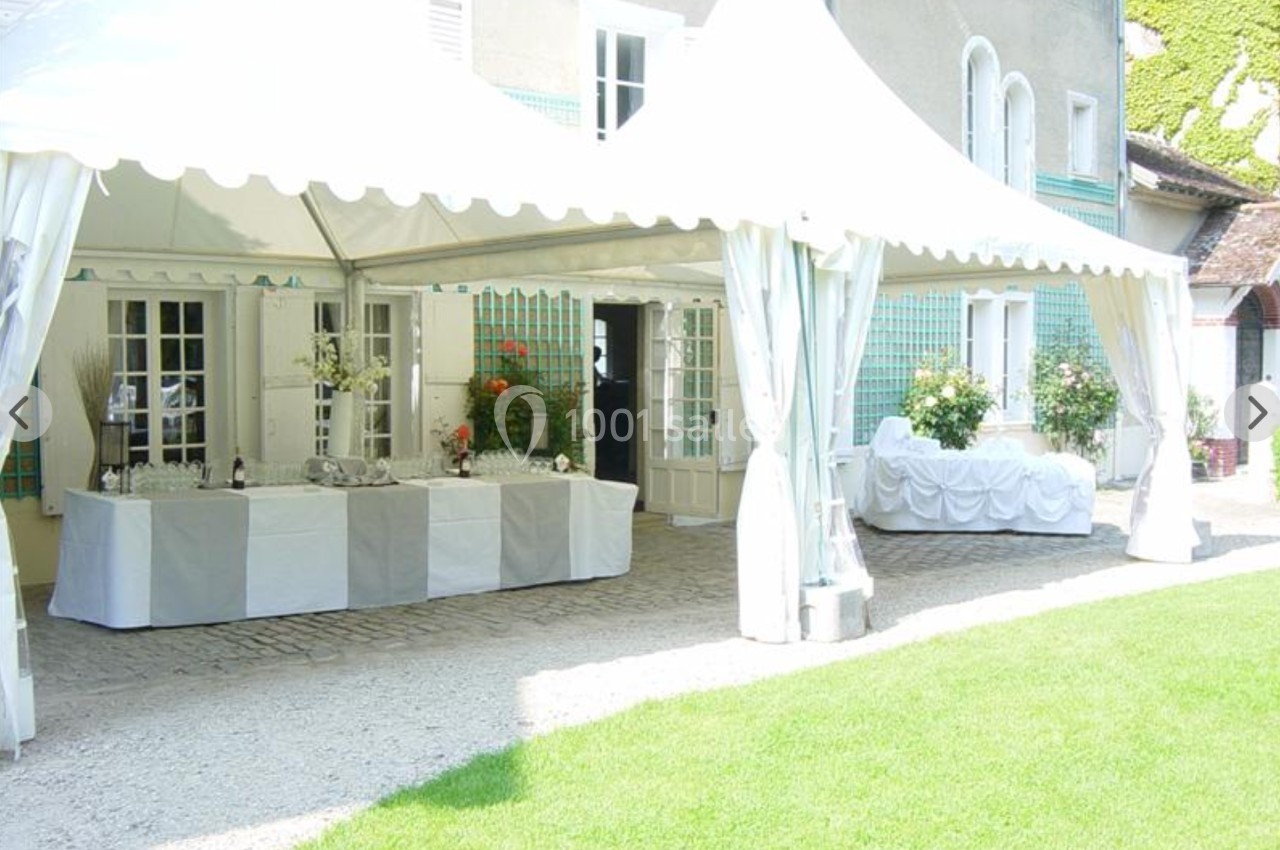Tente blanche installée dans une cour pavée, avec tables dressées et décorations florales.