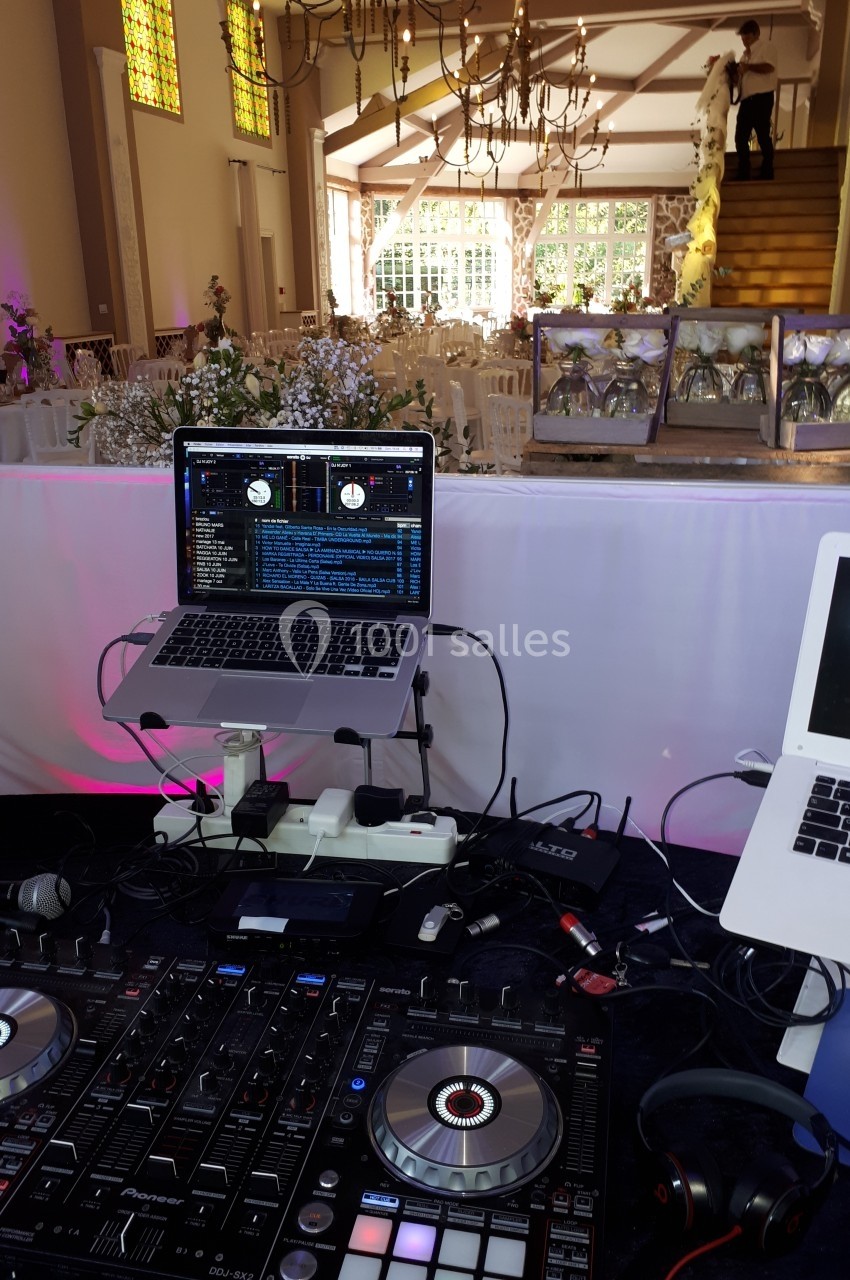 Poste de DJ avec platines et ordinateurs dans une salle de réception décorée pour un mariage.