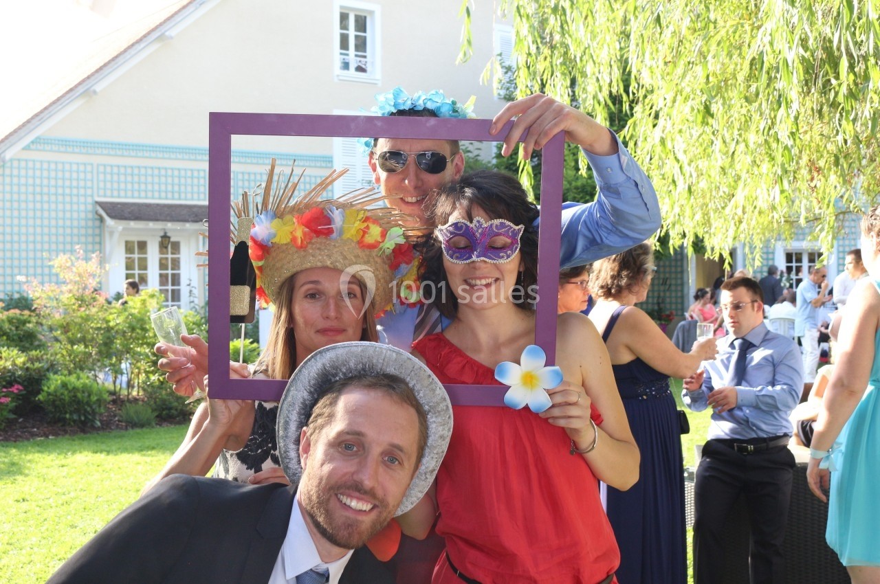 Des personnes souriantes posent avec des accessoires festifs et un cadre violet dans un jardin ensoleillé.