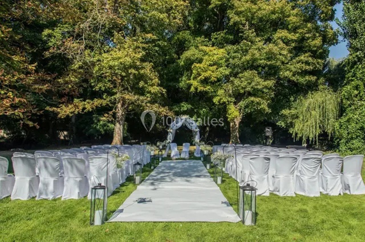 Allée centrale décorée pour une cérémonie de mariage en extérieur, entourée de chaises blanches et d'arbres verdoyants.