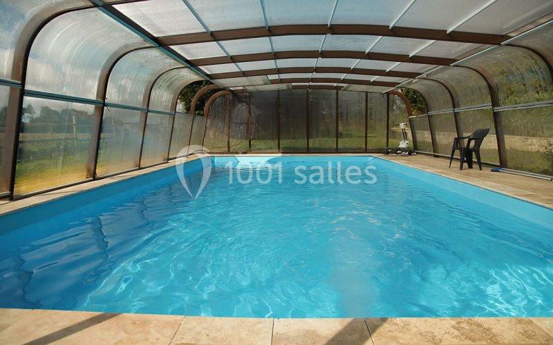 Piscine couverte avec structure transparente, entourée de dalles en pierre et située dans un environnement extérieur.