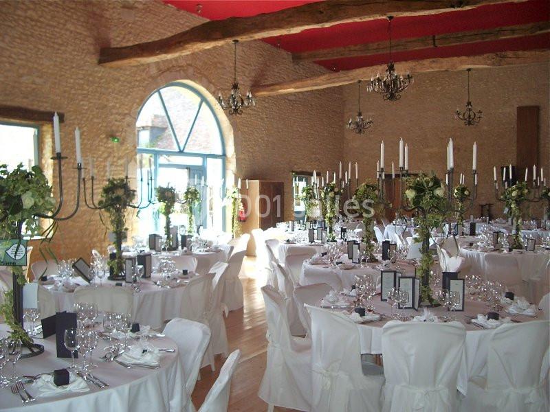 Salle de réception en pierre avec tables dressées, nappes blanches, chandeliers et décorations florales.