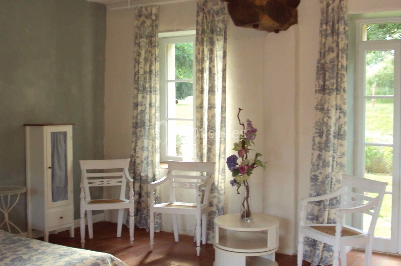 Chambre lumineuse avec murs clairs, mobilier blanc, rideaux à motifs fleuris et sol en carrelage rouge.