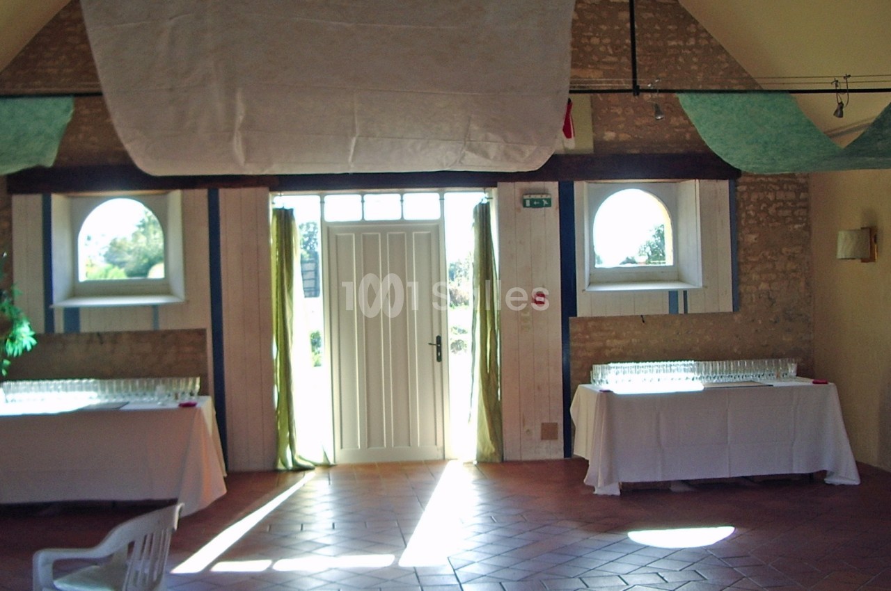 Salle lumineuse avec murs en pierre, tables couvertes de nappes blanches et porte donnant sur l'extérieur.