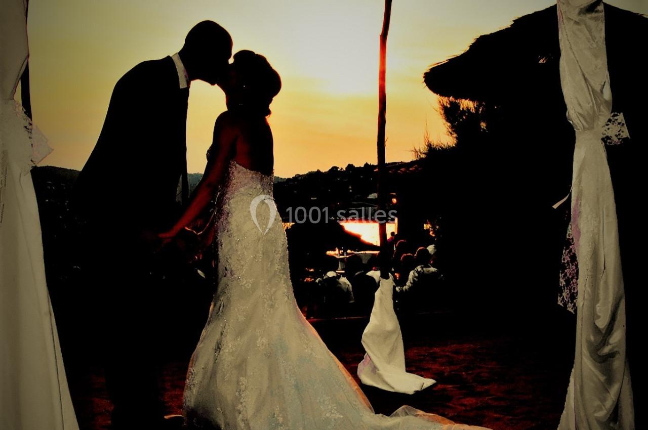 Un couple de mariés s'embrasse sous une arche décorée, au coucher du soleil sur une plage.