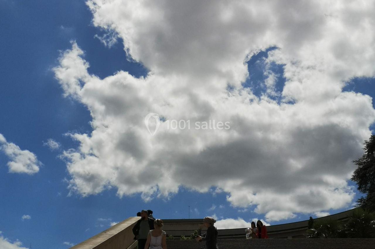 Un couple en tenue de mariage pose sur un large escalier sous un ciel partiellement nuageux.