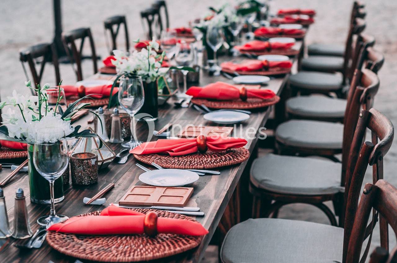 Table dressée en extérieur avec nappes rouges, assiettes blanches, verres et décorations florales.